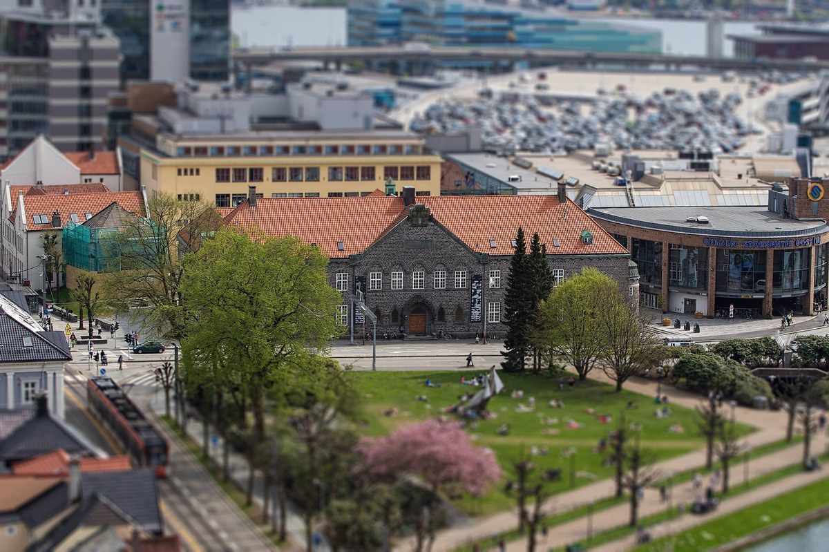 Luftfoto av Bergen Offentlige Bibliotek, en stor murbygning i grå stein med rød teglsteinstak. Bygget har en symmetrisk fasade med mange vinduer og en markert hovedinngang i midten